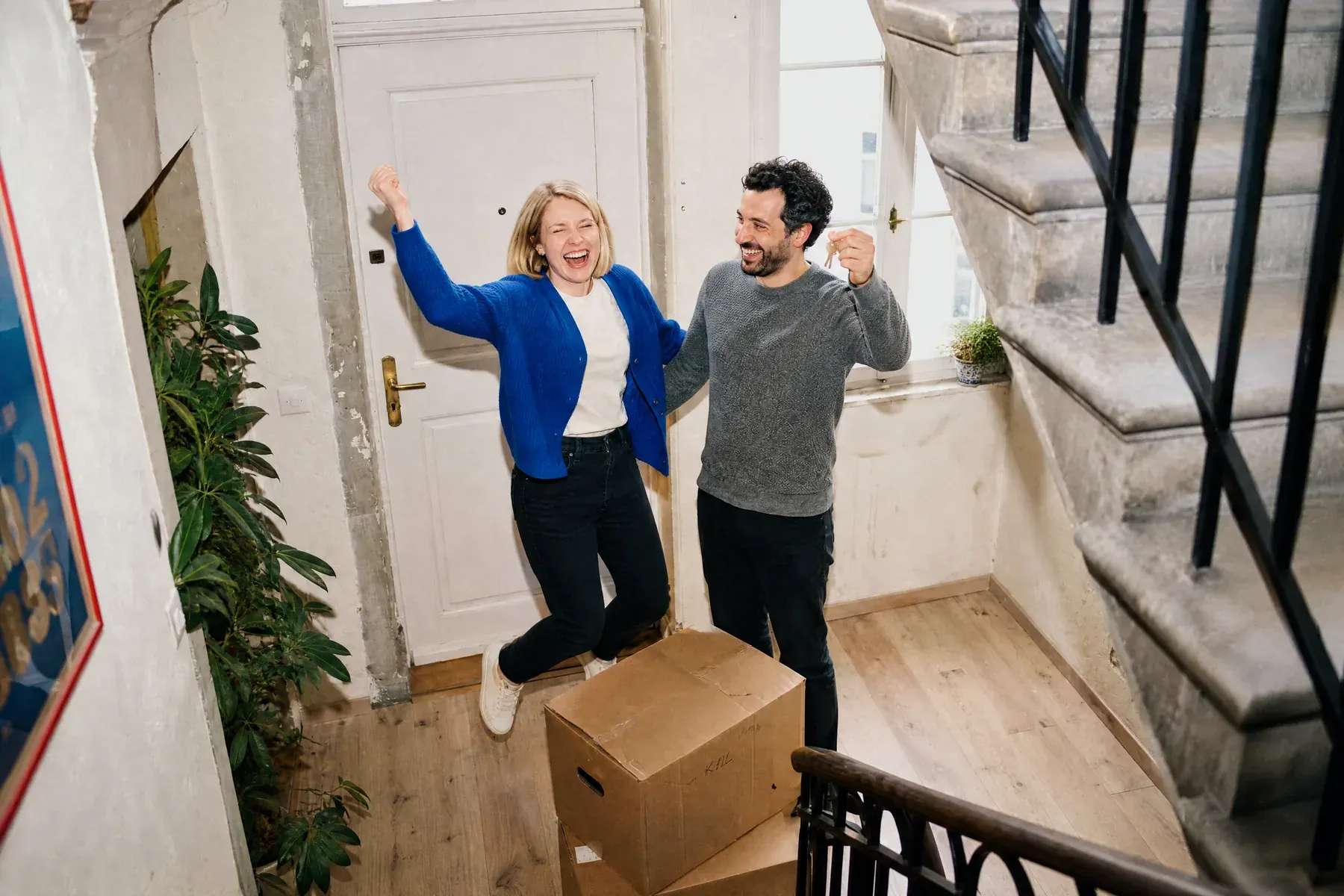 Un couple saute de joie dans l’entrée de son nouvel appartement, entre les cartons.